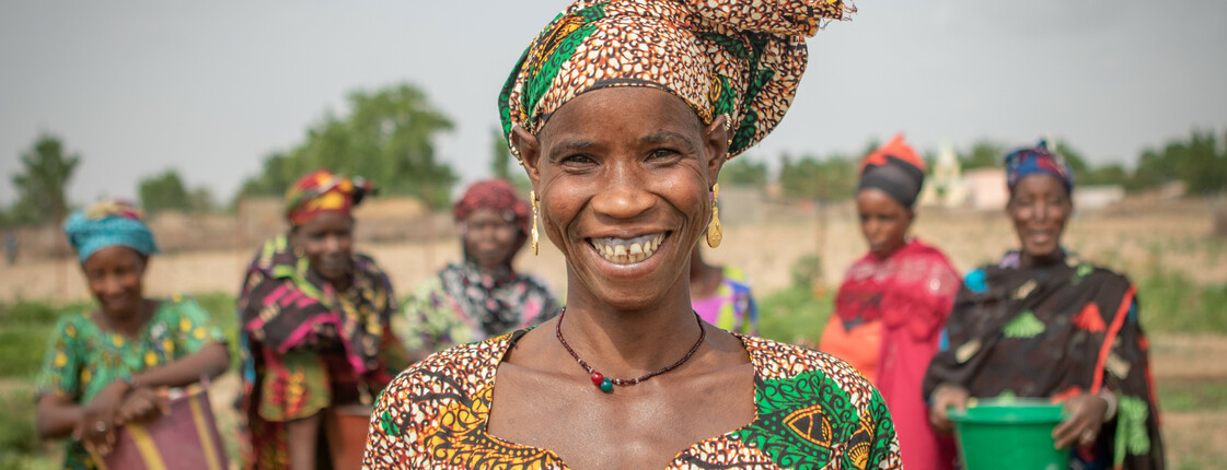 Eine Frau mit buntem Kleid und Kopftuch steht vor einem Bewässerungsbrunnen in der Region Kayes in Mali.