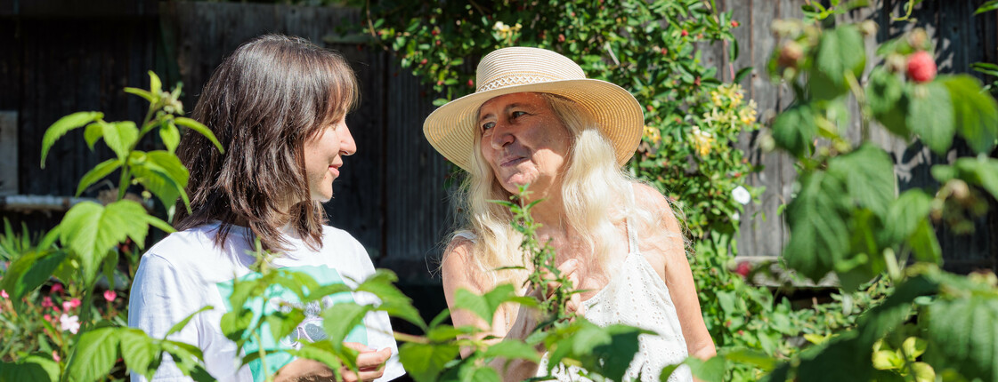 Zwei Frauen, eine trägt einen Strohhut, stehen im Sommer in einem Gemüsegarten. 