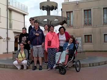 Acht Personen, darunter Menschen mit Behinderung, stehen vor einem historischen Brunnen in Caorle.