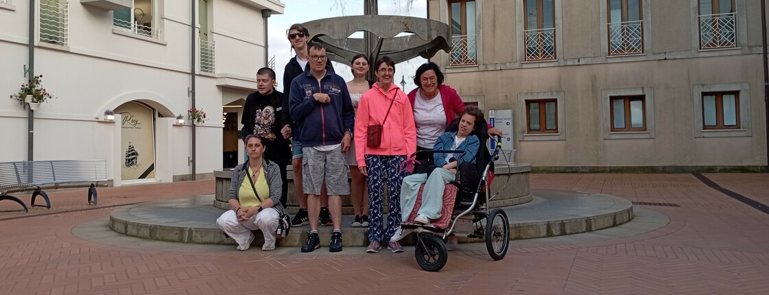 Acht Personen, darunter Menschen mit Behinderung, stehen vor einem historischen Brunnen in Caorle.