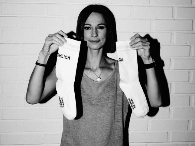 Das Bild zeigt Christina Stürmer, wie sie ein Paar Caritas Karma-Tennissocken in die Kamera hält.