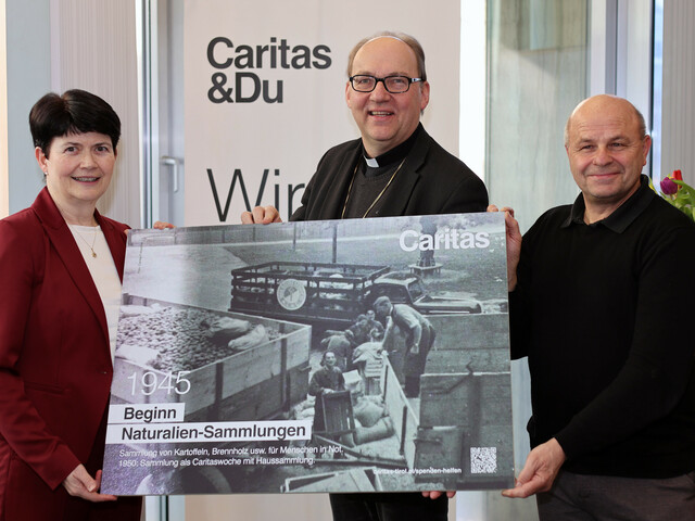 Drei Personen stehen vor einem Caritas Roll-Up und präsentieren ein Plakat mit einer schwaz-weiß Fotografie.