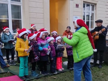 Ein Kinderchor bei dem alle Kinder Nikolausmützen tragen und zwei Personen mittleren Alters mit Gitarren.