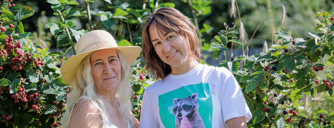 Zwei Frauen in Sommerbekleidung stehen auf einem Feld und halten eine Schüssel Brombeeren in die Kamera.