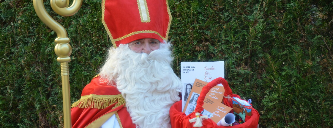 Portrait eines Nikolaus, der vor einer grüner Hecke steht.