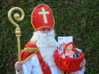 Portrait eines Nikolaus, der vor einer grüner Hecke steht.