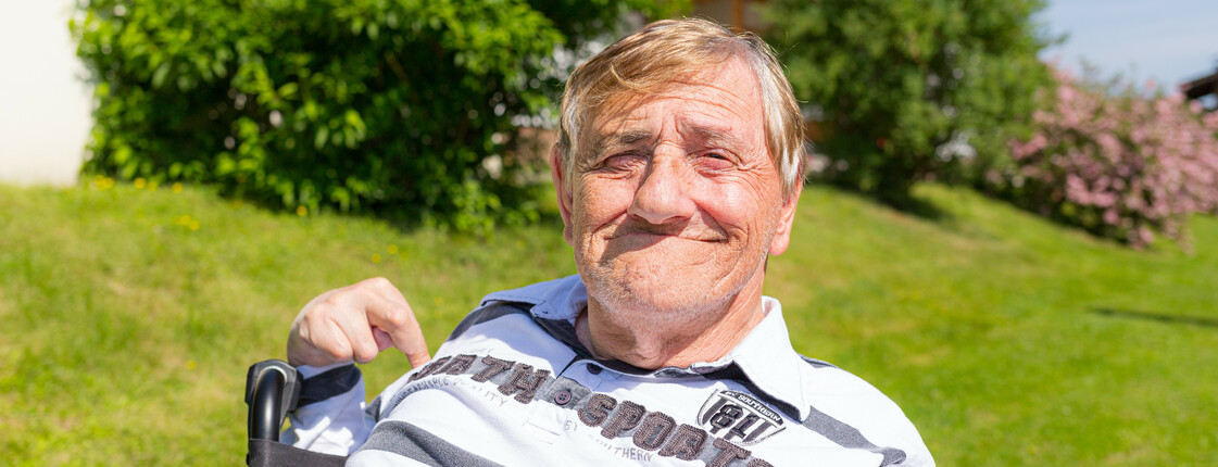 Portrait eines im Rollstuhl sitzenden Mannes in einem grünen Garten.