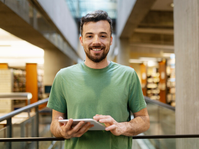 Smiling latin man uses tablet, looks at camera. A middle-aged student studying in library