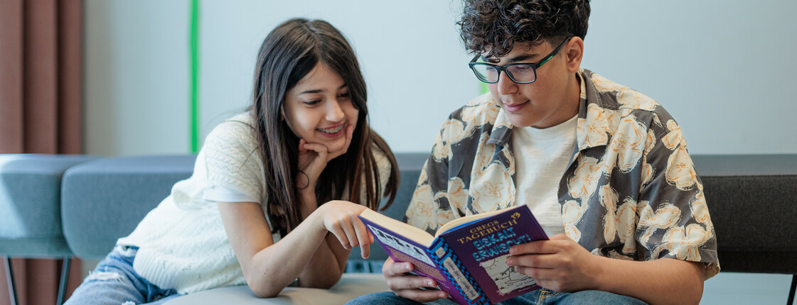 Ein Junge und ein Mädchen sitzen auf einem Sofa und lesen in einem Buch.