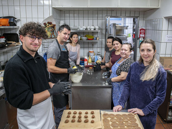 Sieben Personen stehen in einer Gastroküche und backen Weihnachtskeckse.