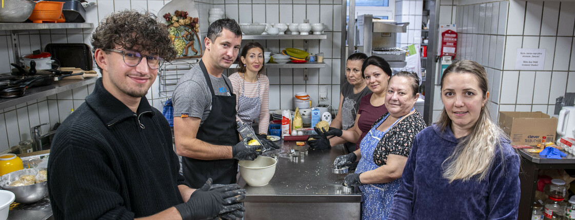 Sieben Personen stehen in einer Gastroküche und backen Weihnachtskeckse.