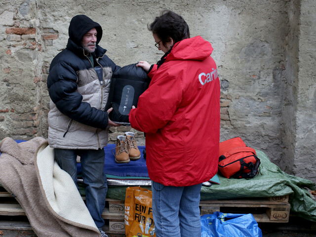 Caritas Streetwork-Mitarbeiterin gibt obdachlosem Menschen einen Schlafsack. 