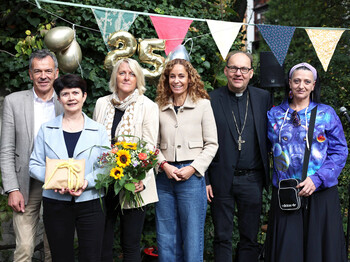 Sechs Perosnen stehen in einem Garten zu einem Gruppenfoto zusammen.