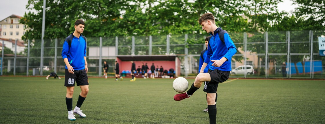 Zwei Jugendliche in blauen Trainingsanzügen spielen auf einem Kunstrasenplatz Fußball.