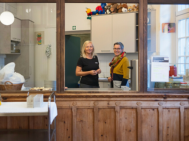 Zwei Frauen stehen in der Katharina-Stube hinter dem Tresen der Essensausgabe.