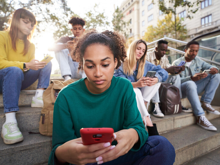 Focused girl looks and types on her phone sitting on city street with friends technology addicted