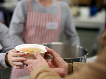 Volunteers serving hot soup for homeless in community charity donation center, coronavirus concept.