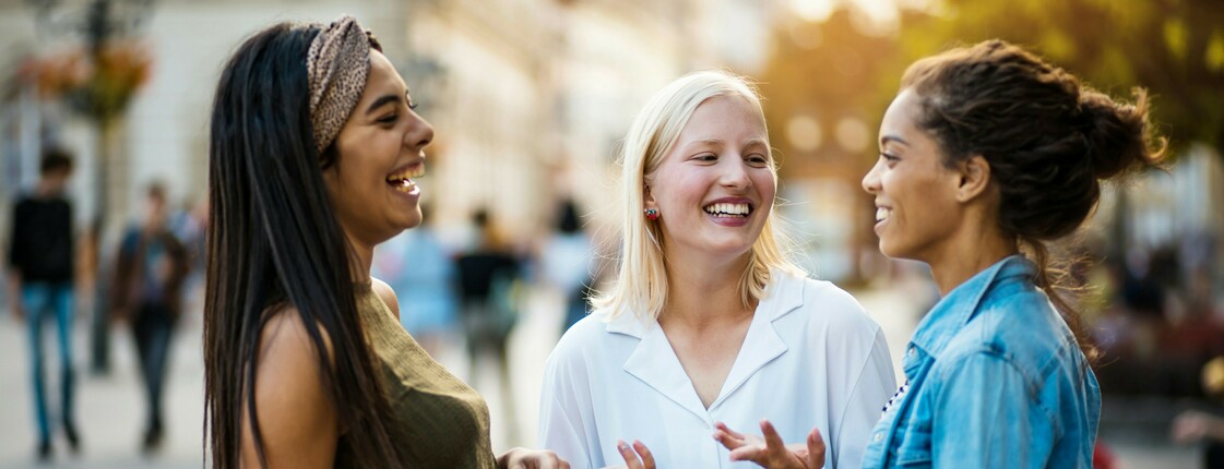 Drei lachende Frauen unterschiedlicher Herkunft unterhalten sich.