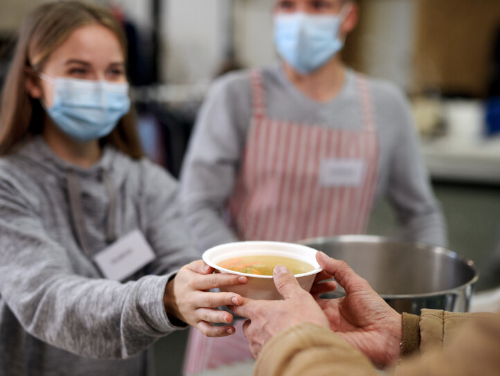 Volunteers serving hot soup for homeless in community charity donation center, coronavirus concept.