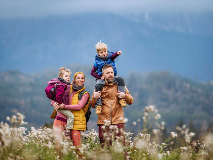 Happy parents with their little kids on piggyback at autumn walk.